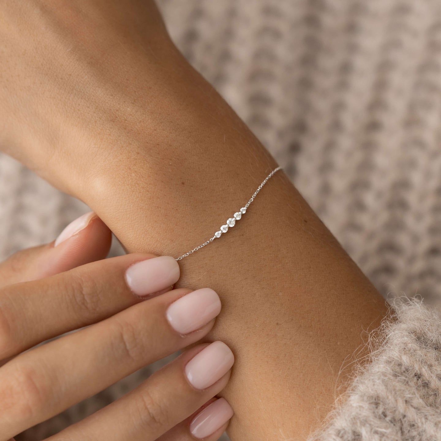 Close-up of a wrist wearing the Graduated Diamond Bracelet White Gold - Tamsin with delicate white gold chain and diamonds