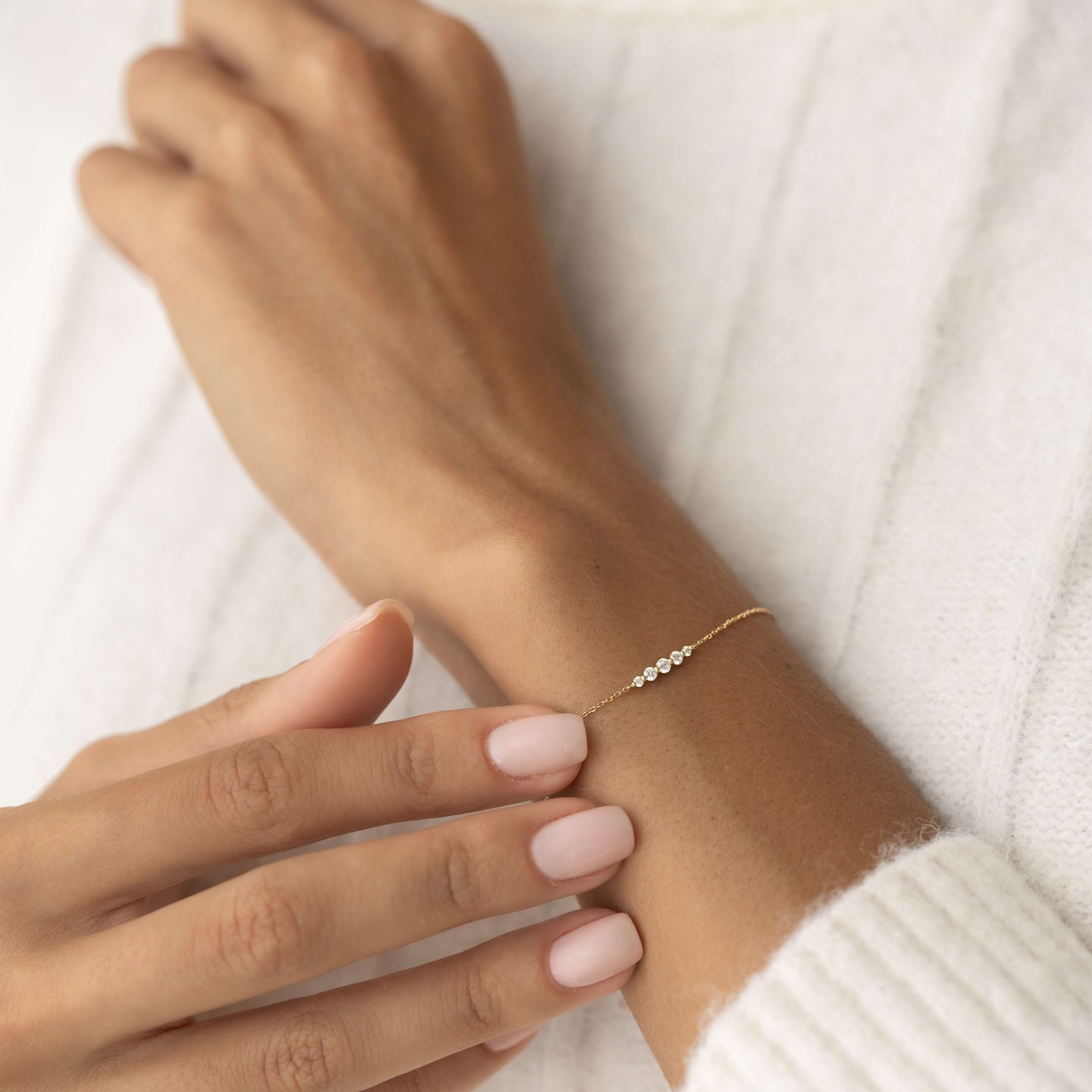 Close-up of a wrist wearing the Graduated Diamond Bracelet 14k Gold - Tamsin with neutral nails and a white sweater background