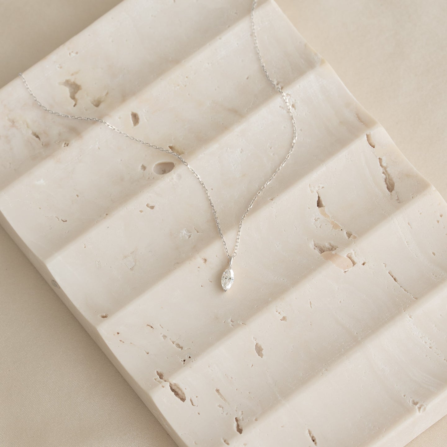 Close-up of a Marquise Diamond Necklace White Gold - Violetta with a delicate chain on a textured beige surface