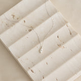 Close-up of a Marquise Diamond Necklace White Gold - Violetta with a delicate chain on a textured beige surface