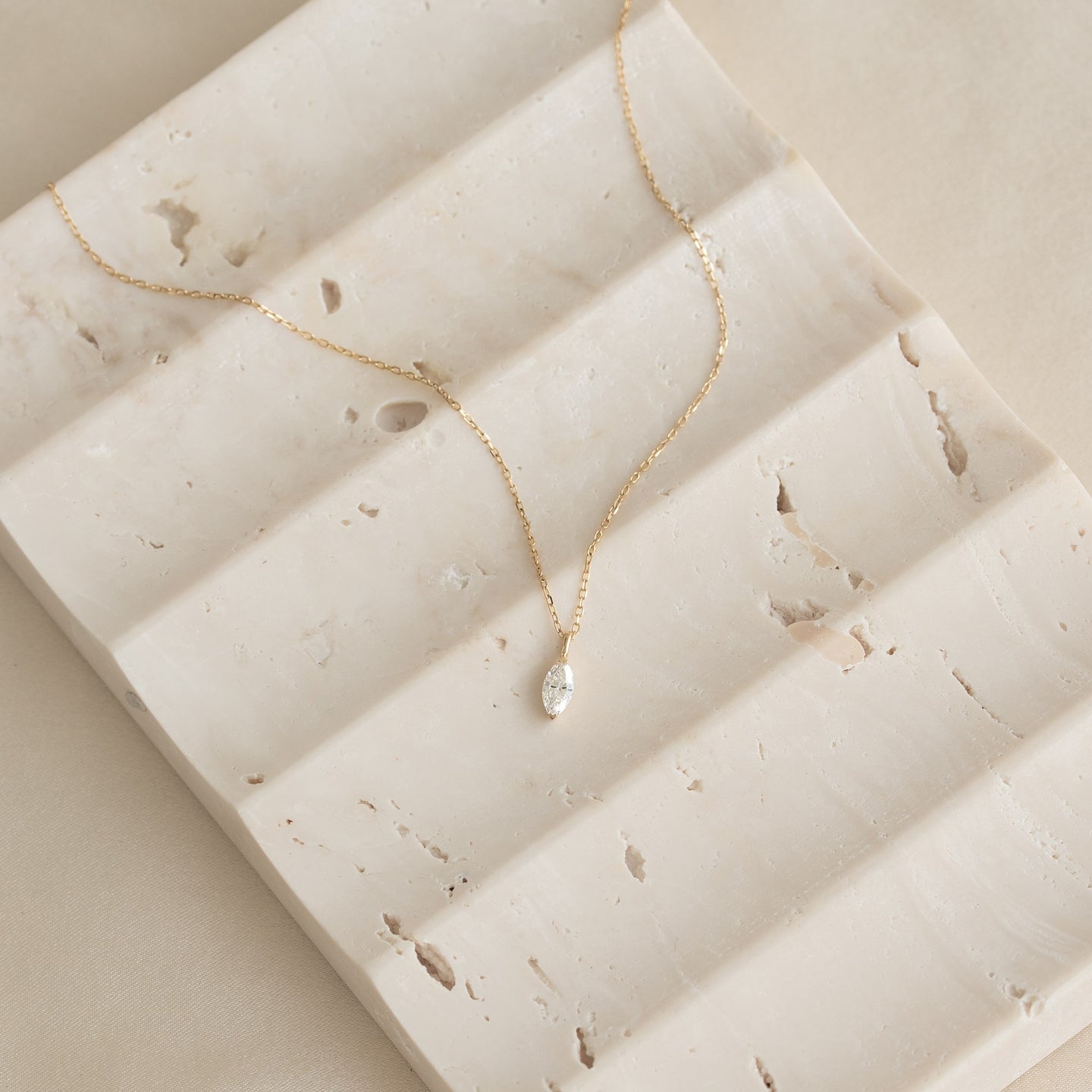 Close-up of Marquise Diamond Necklace 14k Gold - Violetta on textured light beige stone surface with soft natural light