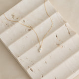 Close-up of Marquise Diamond Necklace 14k Gold - Violetta on textured light beige stone surface with soft natural light