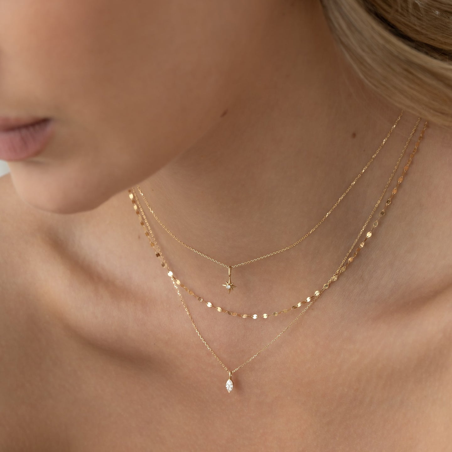 Close-up of a woman wearing the Marquise Diamond Necklace 14k Gold - Violetta layered with delicate gold chains against a neutral background