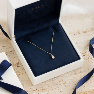 Delicate gold necklace with a teardrop pendant displayed in a white box with navy blue interior lining