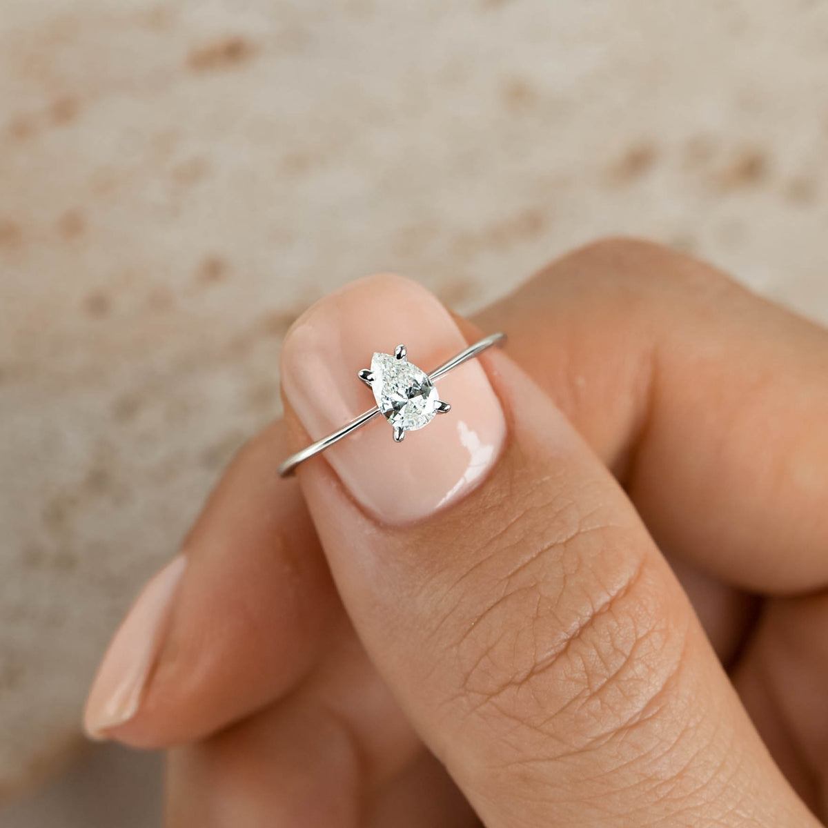 Close-up of a hand holding the Pear Shaped Diamond Ring 14k White Gold - Martine with a delicate band and sparkling diamond