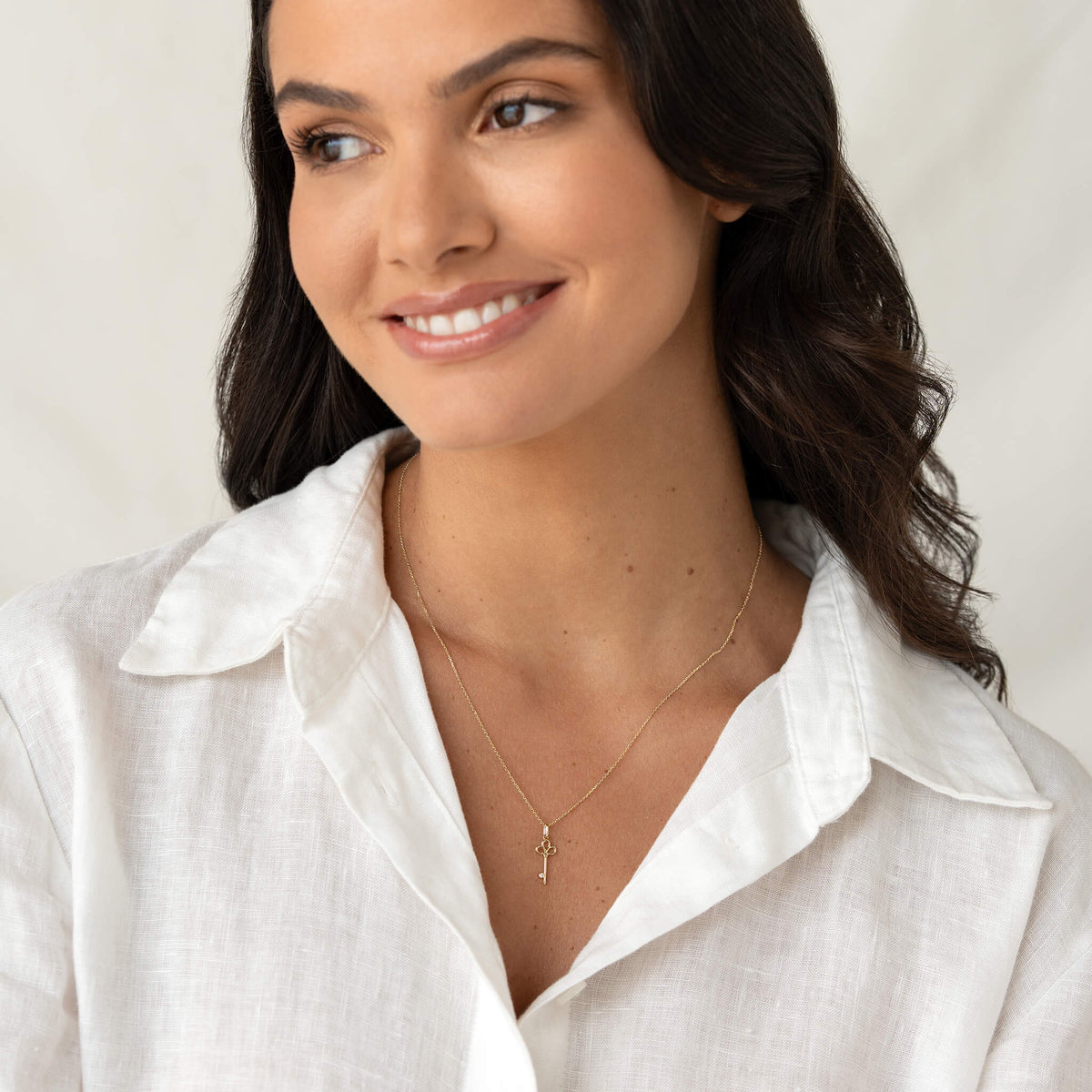 Model wearing a delicate Yellow Gold necklace with a small key shaped pendant, styled with a white collared shirt.