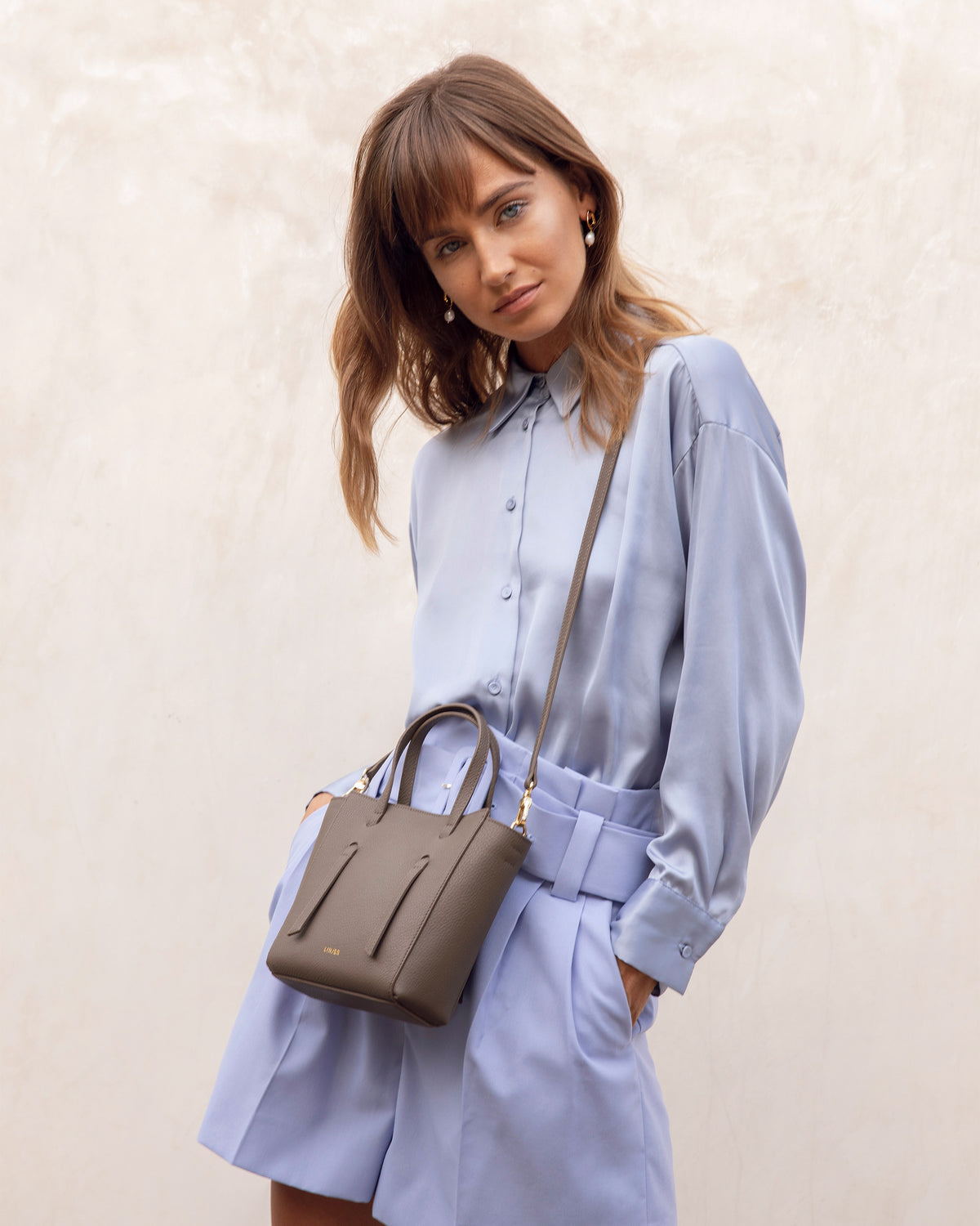 Woman wearing a light blue shirt and shorts styled with The Lana Bag - Blue crossbody mini purse