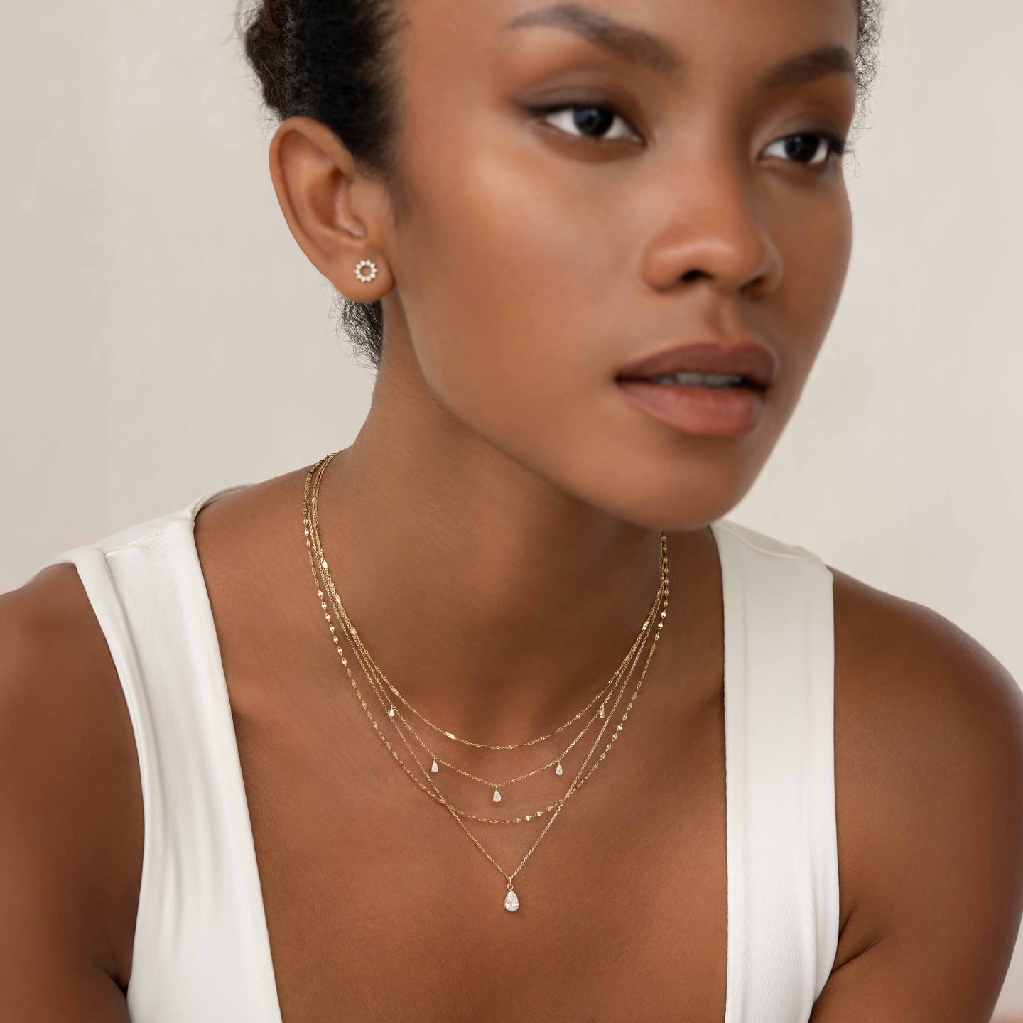 Close-up of woman wearing Pear Cut Diamond Pendant Necklace 14k Gold - Oline with layered delicate gold chains on neutral background