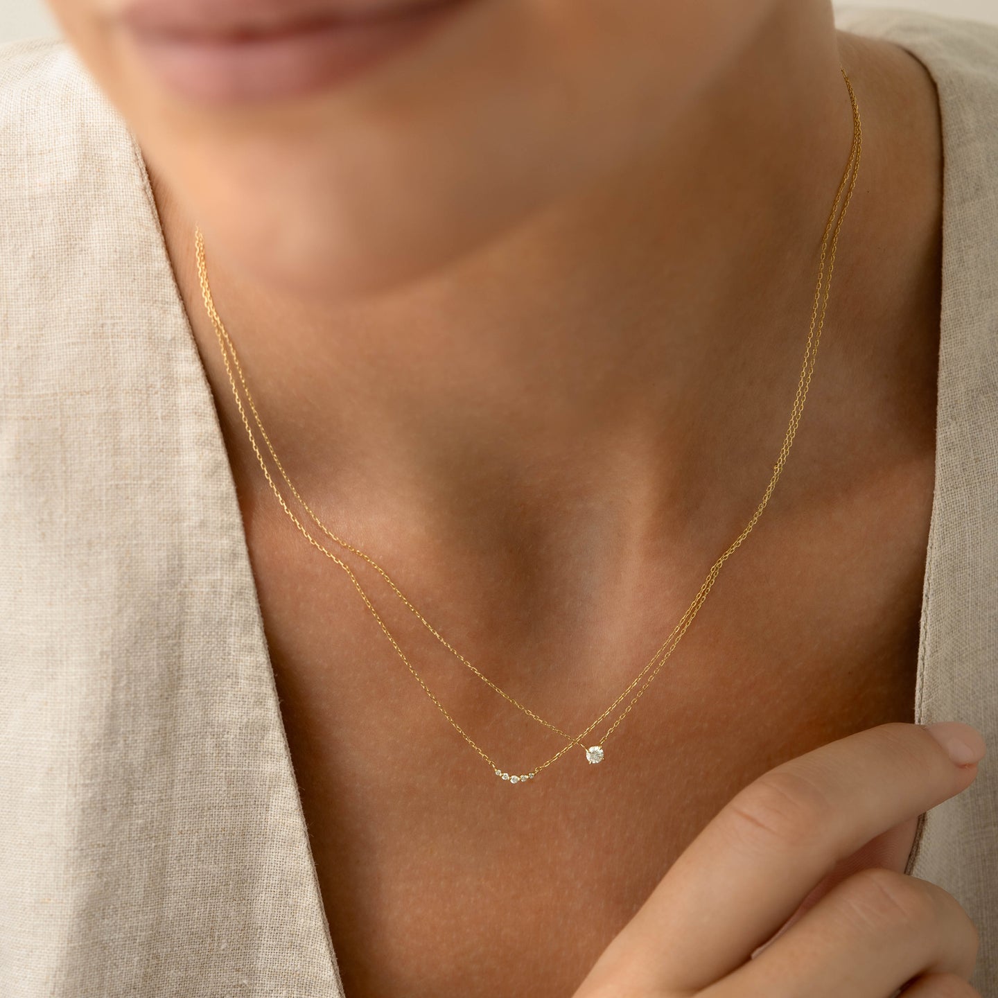 Close-up of a woman wearing the Diamond Pendant Necklace 14k Gold - Johanne with a delicate gold chain on light fabric background