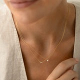 Close-up of a woman wearing the Diamond Pendant Necklace 14k Gold - Johanne with a delicate gold chain on light fabric background