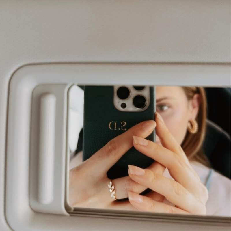 Close-up of a woman taking a mirror selfie showing a silver ring and gold hoop earring with blurred face in the background