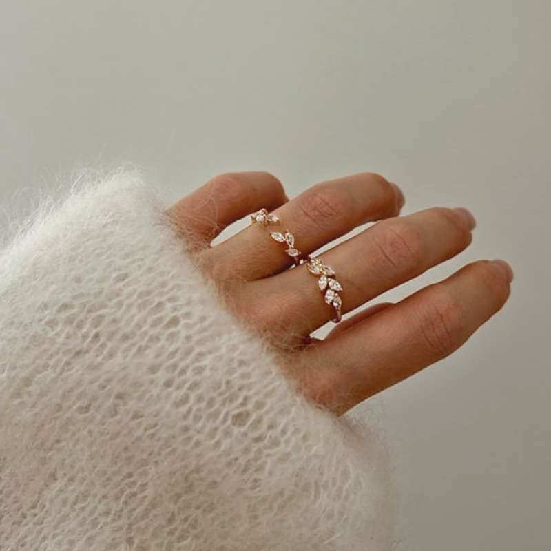 Close-up of a hand wearing two delicate gold rings with leaf-shaped details against a soft beige background