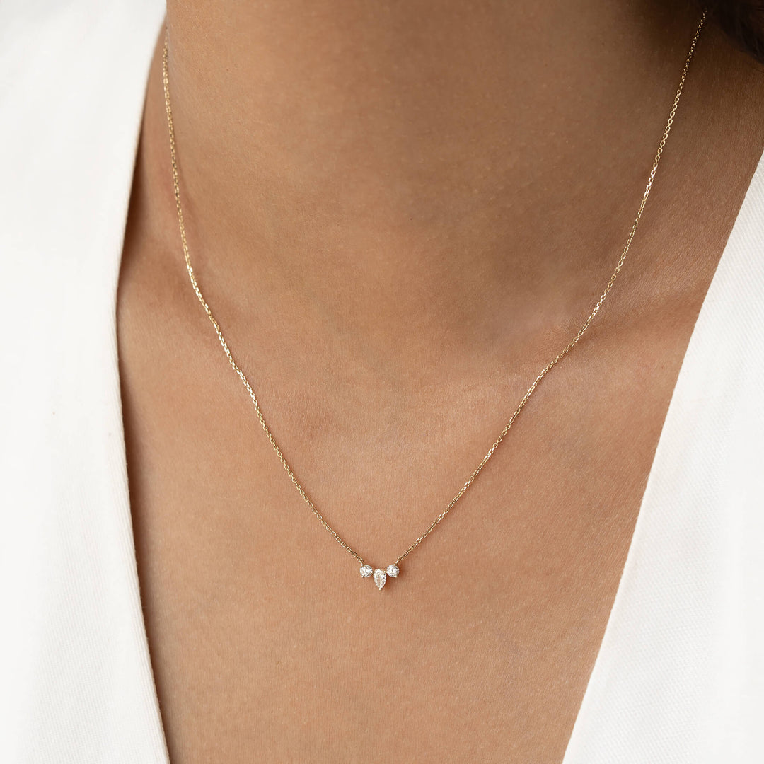 A delicate Gold necklace with three tiny pear-shaped gemstones rests on the neck of a person wearing a V-neck white top, conveying elegance and simplicity.