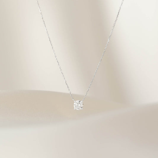 Close-up of a delicate White Gold chain necklace with a single round diamond pendant in a prong setting, centered against a soft neutral background.