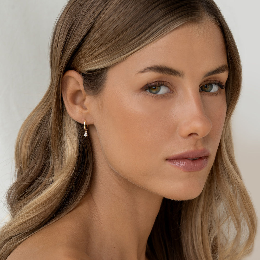 A model features a stylish and luxurious 14k gold huggie earrings with pear-cut diamond drops.
