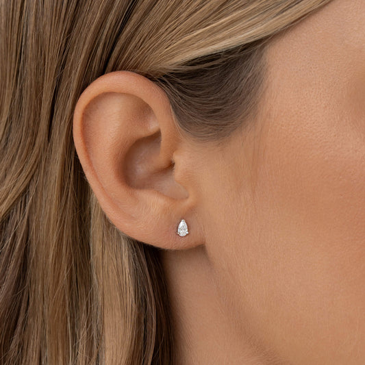 A close-up of a woman's ear adorned with a small, White Gold elegant pear-shaped diamond stud earring.