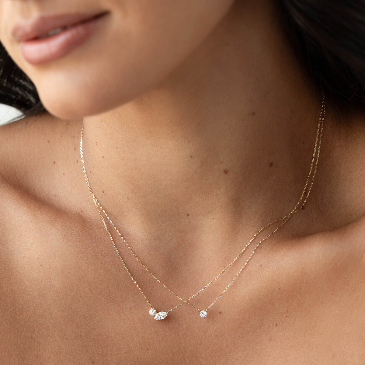 Close-up of layered Gold necklaces featuring small round and marquise-cut gemstone pendants on a woman’s neck.