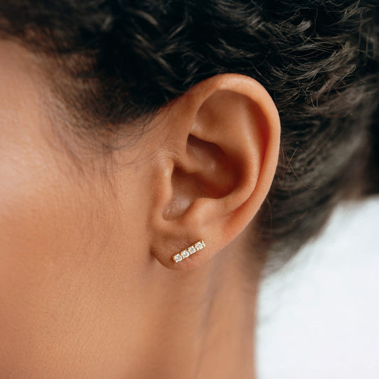 Close-up of a woman wearing 14k Yellow Gold Diamond Bar Stud Earrings - Lucia with four brilliant diamonds on the earlobe