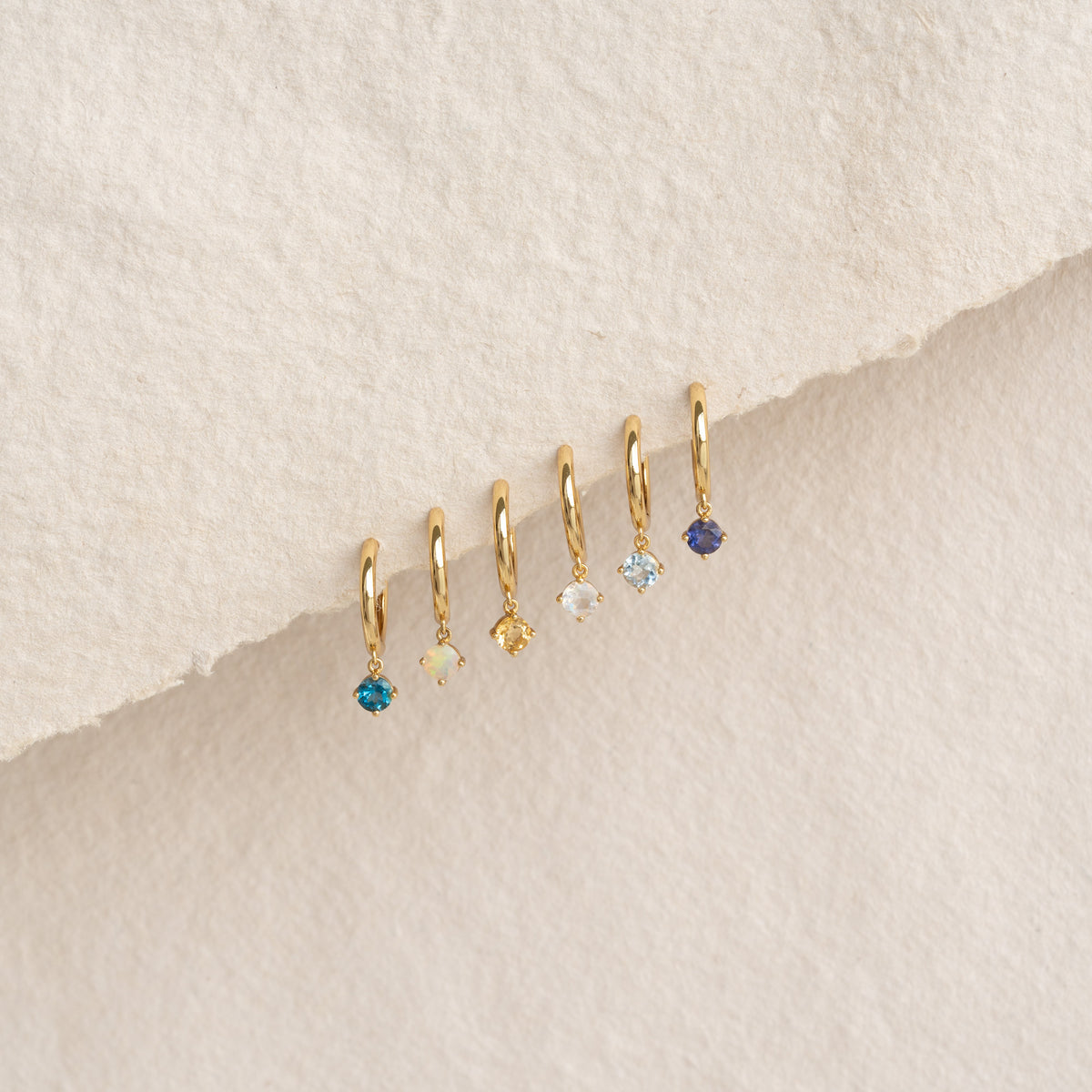 Close-up of March Birthstone Drop Huggie Earrings - Aquamarine with gold vermeil and pastel gemstone drops on textured background