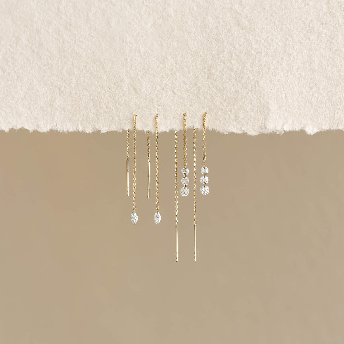 Gold delicate chain earrings hang from textured white paper, featuring elegant, sparkling gemstones, set against a neutral background.