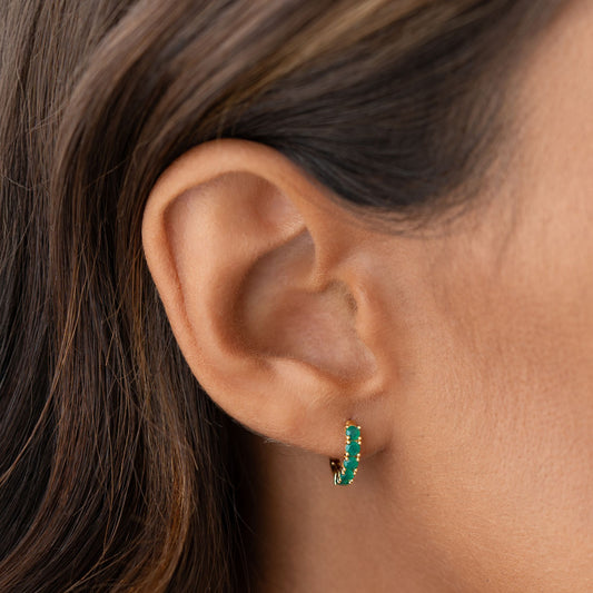 Close-up of an ear wearing May Birthstone Huggie Earrings - Green Chalcedony with small green stones set in gold vermeil