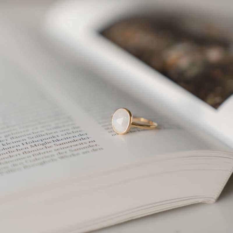 Close-up of a gold ring with a smooth white stone resting on the open pages of a book with soft lighting