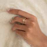 Close-up of a hand wearing the Oval Morganite and Diamond Ring 14k Gold - Demetria on a soft cream fabric background