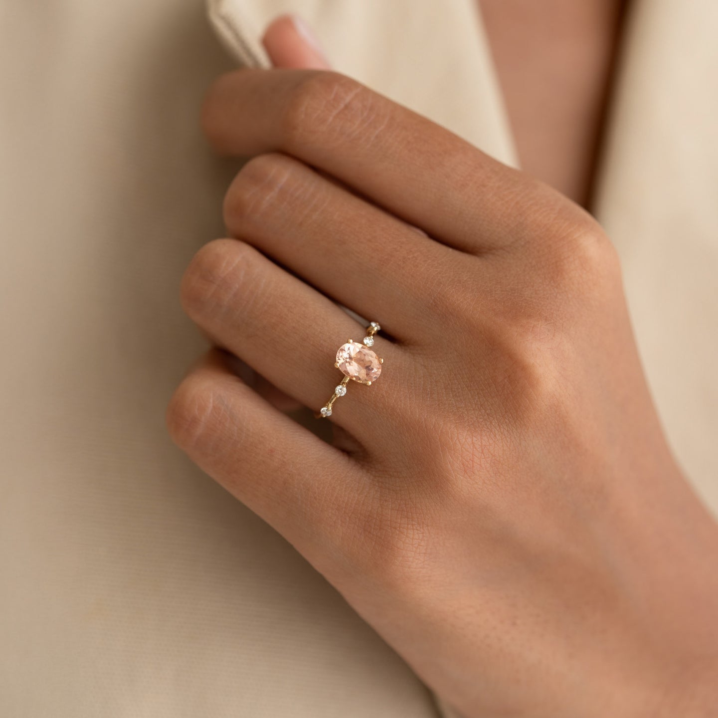 Close-up of hand wearing Oval Morganite and Diamond Ring 14k Gold - Demetria with soft beige fabric background