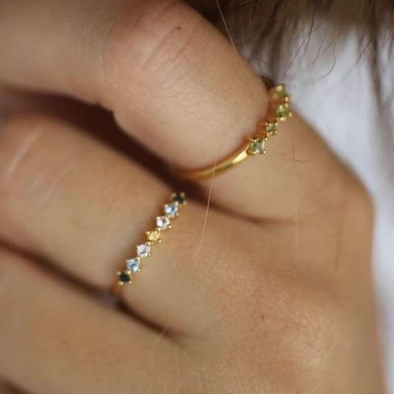 Close-up of two delicate gold rings with small clear stones worn on a person's fingers against a neutral background