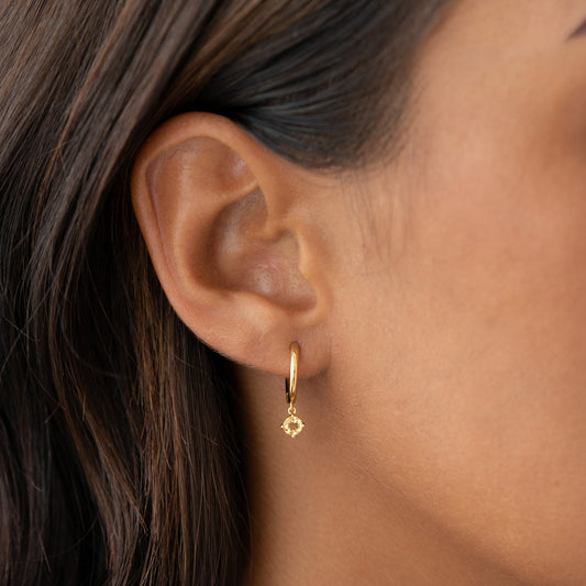 Close-up of ear wearing November Birthstone Drop Huggie Earrings - Citrine with gold vermeil setting on neutral background