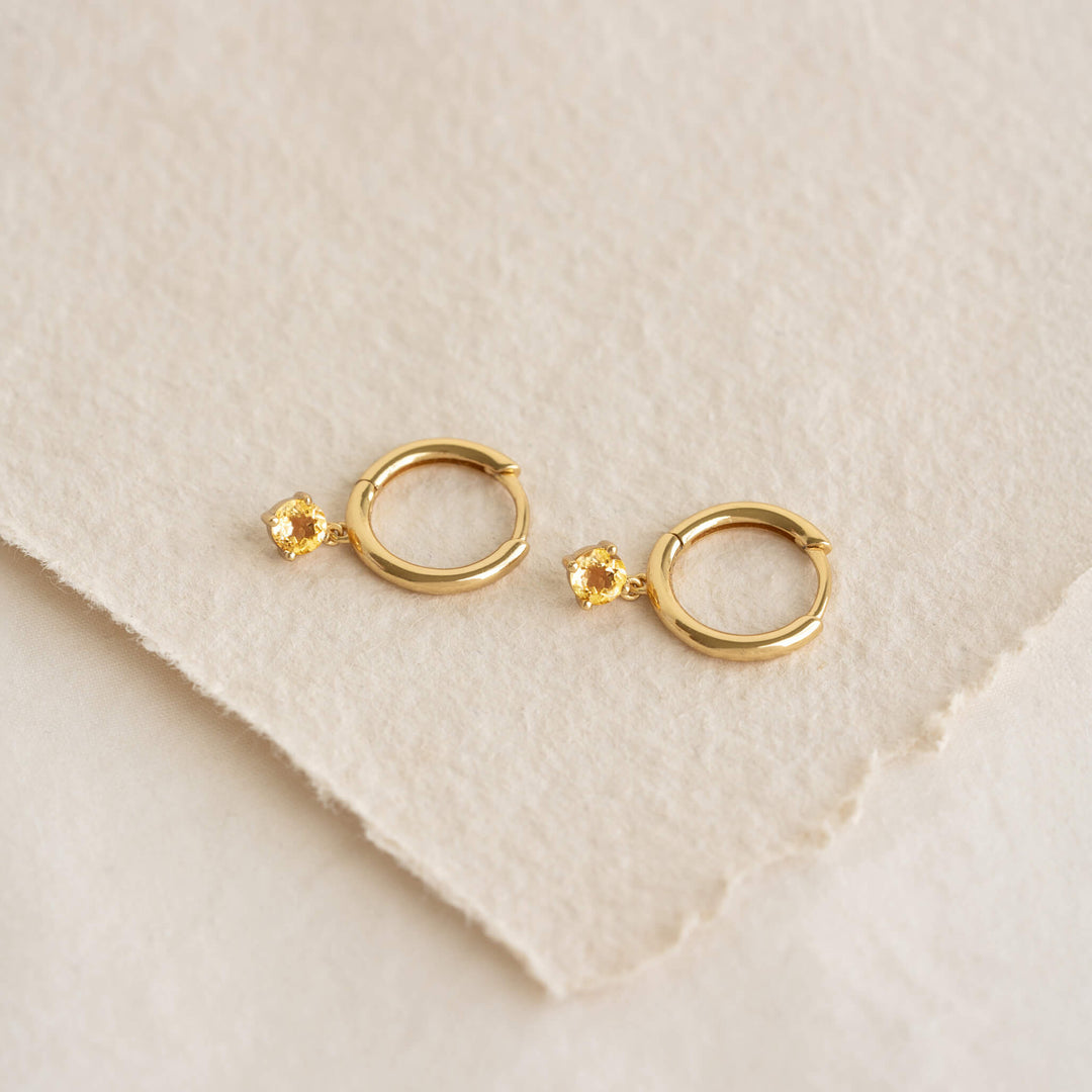 Close-up of November Birthstone Drop Huggie Earrings - Citrine with gold vermeil setting on cream textured background
