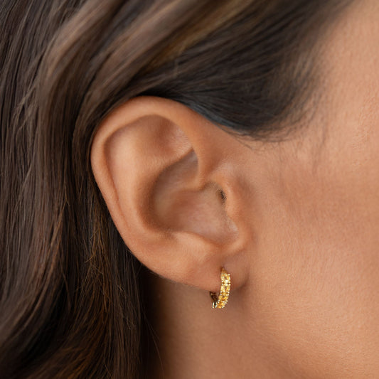 Close-up of a woman wearing November Birthstone Huggie Earrings - Citrine with gold vermeil setting on neutral background