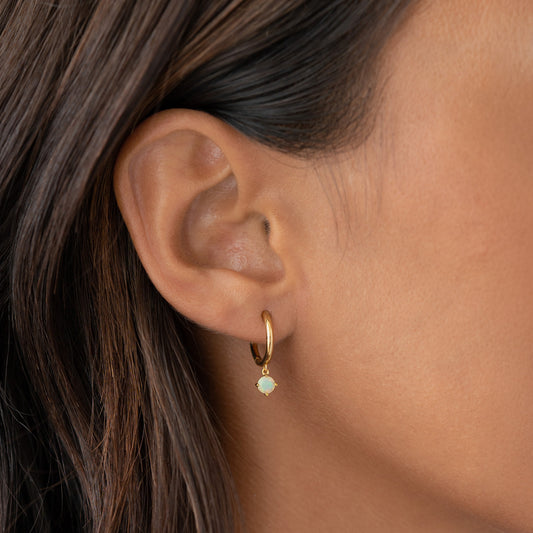 Close-up of a woman wearing October Birthstone Drop Huggie Earrings - Opal with gold vermeil and Ethiopian opal charm