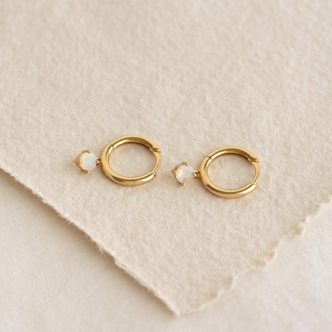 October Birthstone Drop Huggie Earrings - Opal with gold vermeil setting on textured beige background