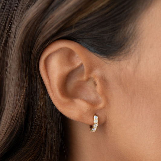 Close-up of an ear wearing October Birthstone Huggie Earrings - Opal with gold vermeil and vibrant opal stones