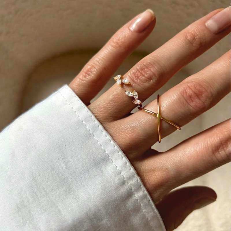 Close-up of a hand wearing two delicate gold rings, one with small gems and one with a minimalist crisscross design