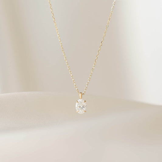 A delicate Gold necklace featuring a fine chain and a small oval-cut diamond pendant. The diamond is set in a simple prong setting, allowing it to catch and reflect light subtly.