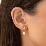 Close-up of an ear wearing Pearl Drop Earrings - Ariana with baroque pearl and floral cubic zirconia details on a light background