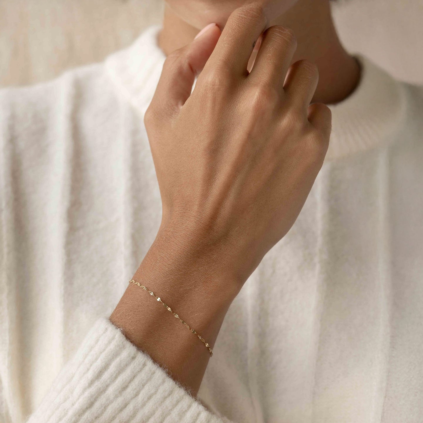 Close-up of a hand wearing the Petal Chain Bracelet 14k Gold - Florence on a white textured sweater background