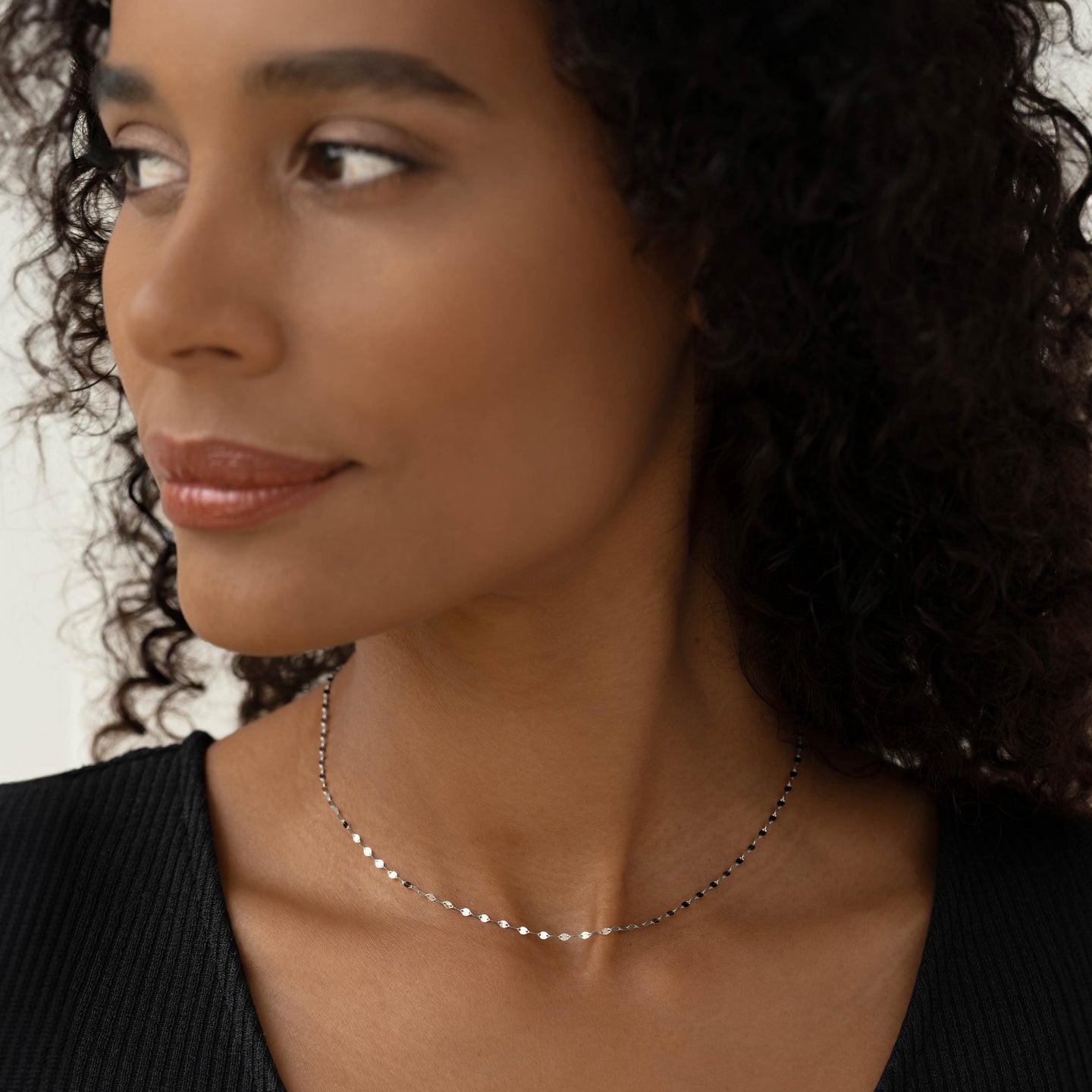 Close-up of a woman wearing the 14k White Gold Petal Chain Necklace - Fleur with intricate petal-shaped links and black top