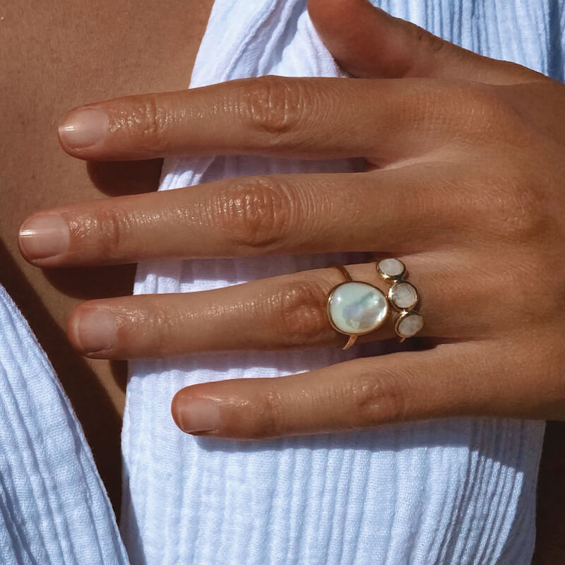 Close-up of a hand wearing two gold rings with white stones on fingers against a white textured fabric background