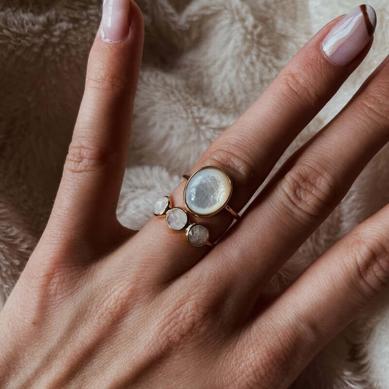 Close-up of a hand wearing a gold ring with four white moonstone gems resting on a soft beige fabric background