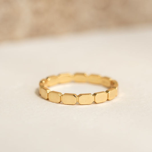 Close-up of a Ribbed Gold Ring - Mika with geometric linked segments in warm gold on a neutral beige background