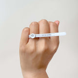 Hand wearing a white Ring Sizer wrapped around the finger against a neutral light background