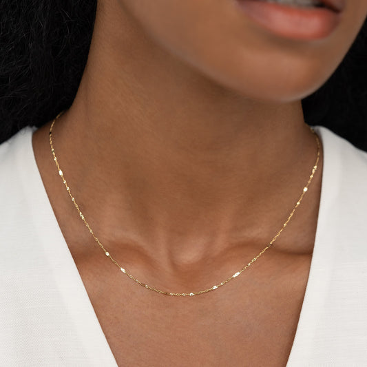 Close-up of a woman wearing the Shimmer Chain Necklace 14k Gold - Clara with a subtle sparkle on a white top