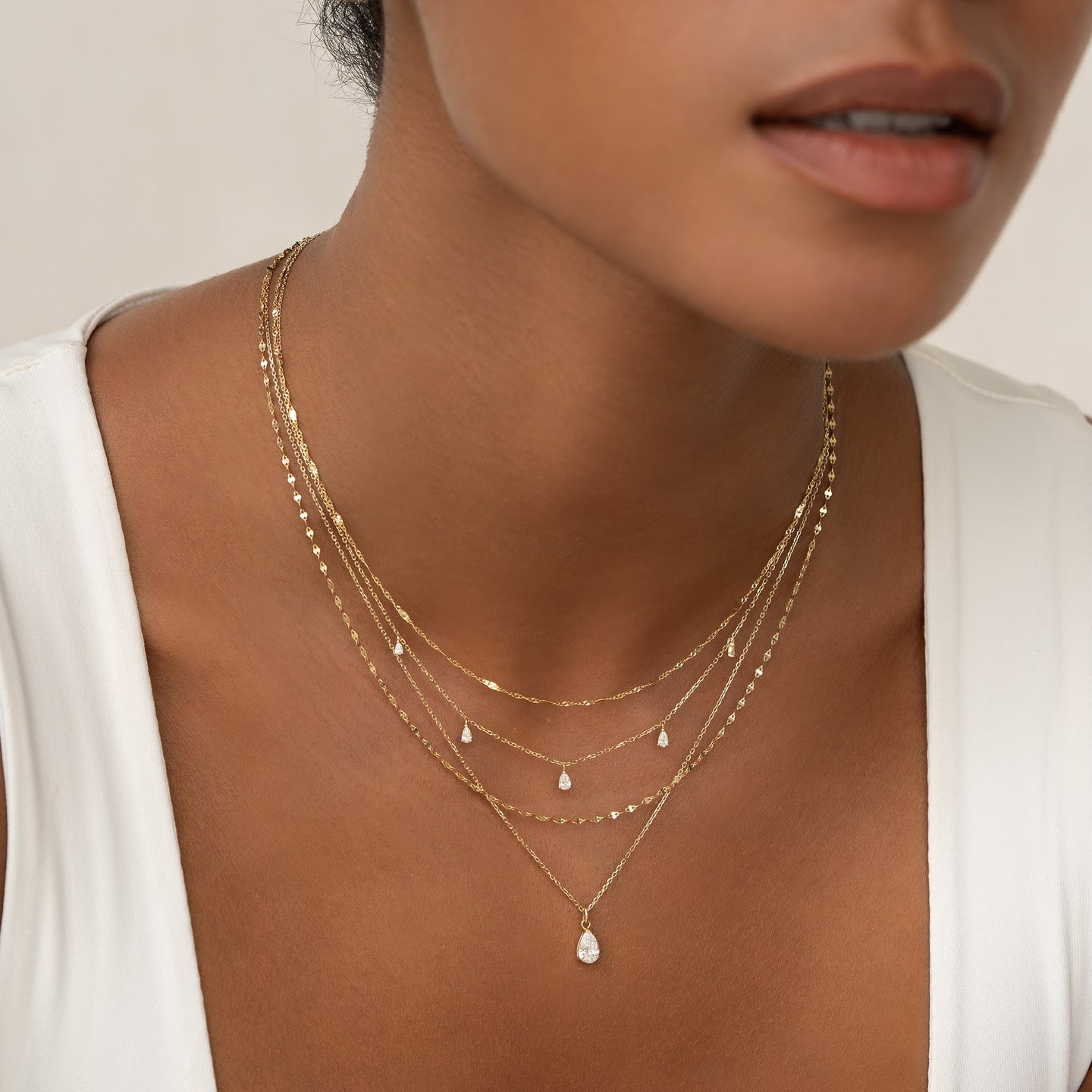 Close-up of a woman wearing layered Shimmer Chain Necklace 14k Gold - Clara with delicate drop accents on a neutral background