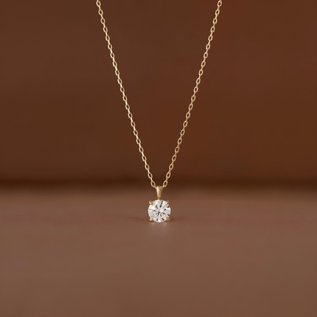 A close-up shot of a delicate White Gold necklace featuring a brilliant, pear-shaped diamond pendant suspended from a fine link chain against a soft, neutral brown-colored background.