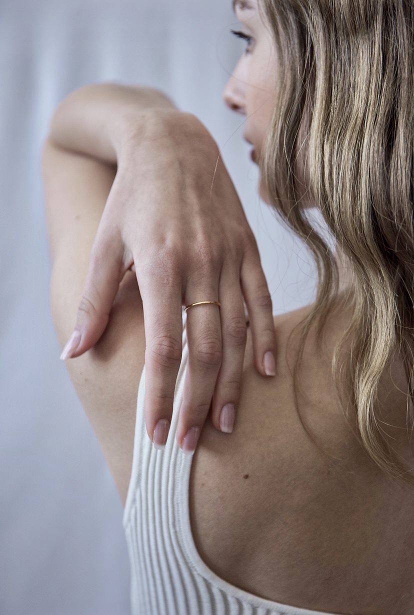 Close-up of a woman with natural makeup wearing a thin gold ring on her finger and a white ribbed tank top