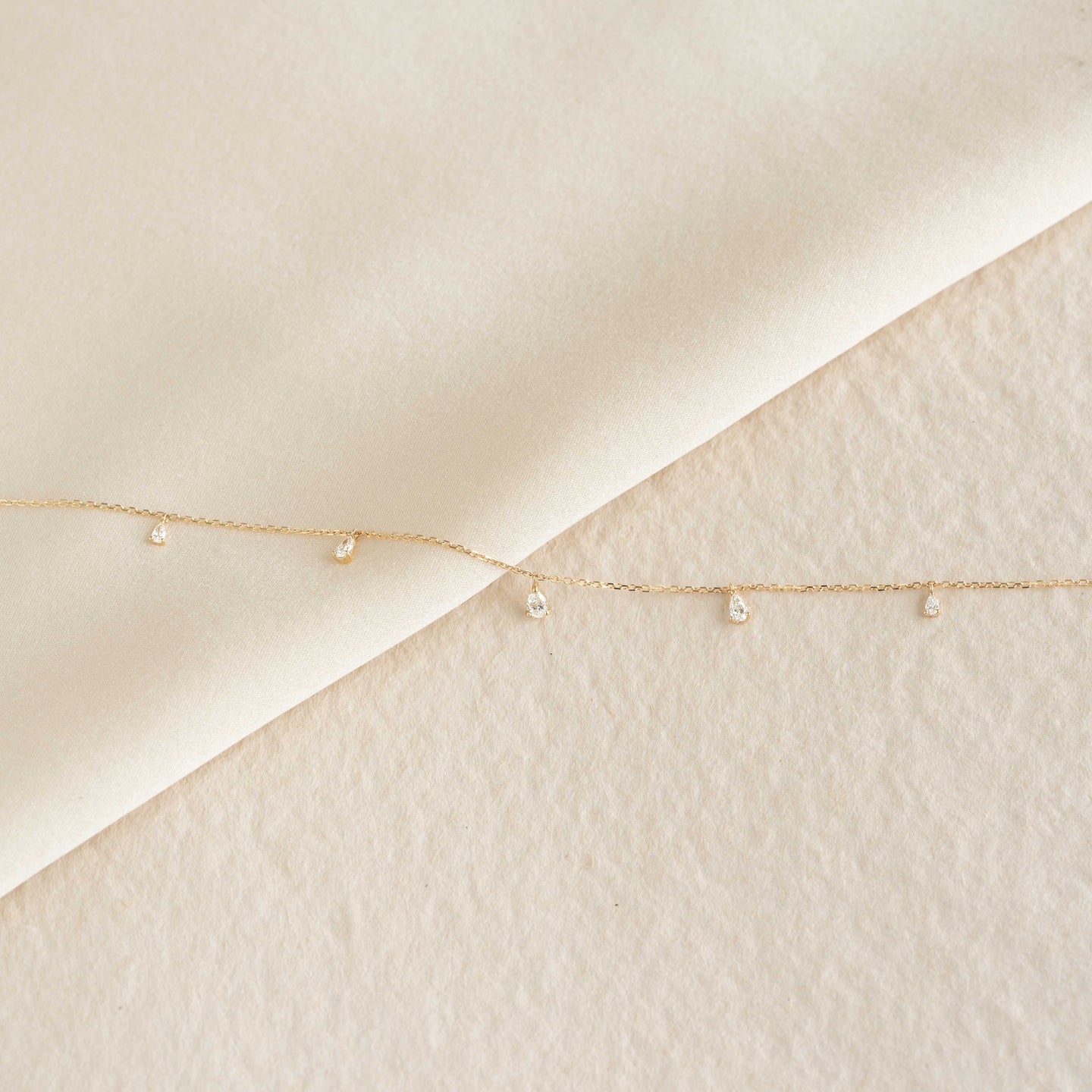 Close-up of Pear Cut Diamond Pendant Necklace 14k Gold - Sylvie with small diamonds on delicate gold chain on cream background