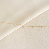 Close-up of Pear Cut Diamond Pendant Necklace 14k Gold - Sylvie with small diamonds on delicate gold chain on cream background